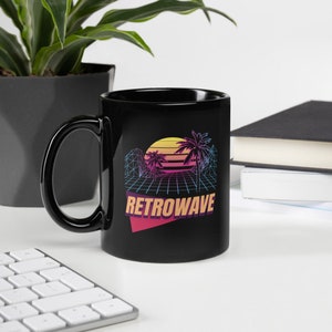 Puede incluir: Taza de cerámica negra con un diseño retro-wave que presenta una puesta de sol, palmeras y un patrón de cuadrícula. El texto "RETROWAVE" está impreso en una fuente colorida y estilizada.