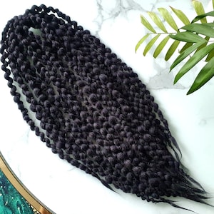 May include: A bundle of black crochet braids, also known as faux locs, on a white marble surface.