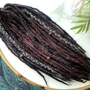 May include: A set of brown and black synthetic dreadlocks with brown beads. The dreadlocks are arranged in a circle on a white surface.