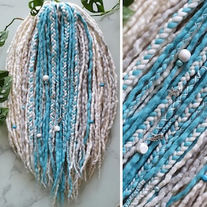 May include: A set of synthetic dreadlocks in white and turquoise blue. The dreadlocks are decorated with white beads and silver charms.