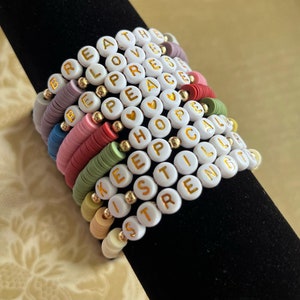 May include: A stack of colorful beaded bracelets with white letter beads spelling out positive messages like "breathe", "love", "peace", "hope", "keep", "still", and "strength".