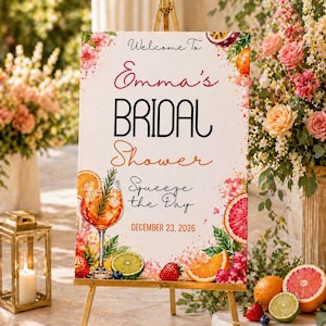 Könnte beinhalten: Ein Schild auf einer goldenen Staffelei mit der Aufschrift "Welcome To Emma's Bridal Shower" mit dem Satz "Squeeze the Day" und dem Datum 23. Dezember 2026. Das Schild ist mit Blumen- und Fruchtdarstellungen dekoriert, darunter Orangen, Erdbeeren und ein Cocktail.