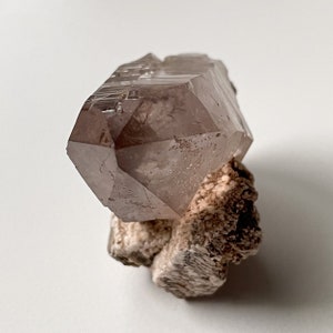 May include: A large, clear, pink quartz crystal with a double termination. The crystal is sitting on a bed of white, brown, and gray matrix.