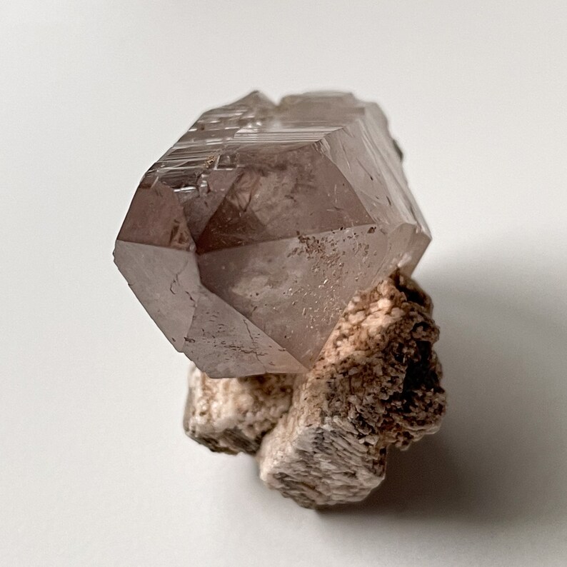 May include: A large, clear, pink quartz crystal with a double termination. The crystal is sitting on a bed of white, brown, and gray matrix.