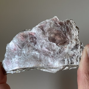 Op de afbeelding: Een groot, onregelmatig gevormd stuk mica met een zilvergrijze kleur en een subtiele roze tint. De mica heeft een gelaagde, schilferige textuur.