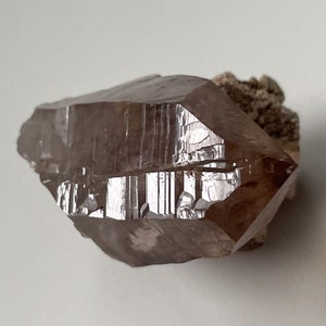 May include: A large, smoky quartz crystal with a pointed tip and striations on its surface. The crystal is brown and translucent, with a slight reddish hue.