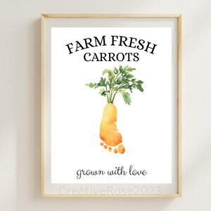 May include: Framed print with a watercolor illustration of a carrot shaped like a footprint, with green leafy tops. The text "FARM FRESH CARROTS" is above the carrot, and "grown with love" is below. The frame is light brown.