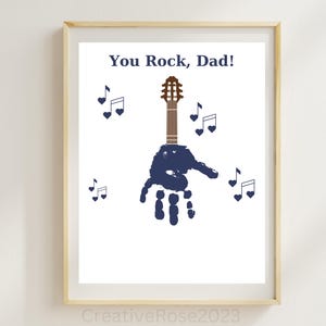 May include: A framed print with the text "You Rock, Dad!" and a blue handprint holding a brown guitar with musical notes around it.