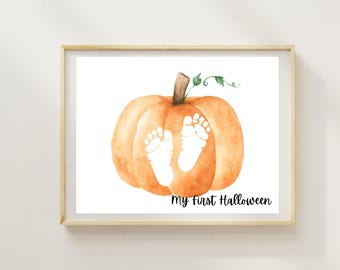Könnte beinhalten: Ein gerahmter Aquarelldruck mit einem orangefarbenen Kürbis mit weißen Babyfüßen. Der Text "My First Halloween" ist in schwarzer Schrift unter dem Kürbis geschrieben. Das Kunstwerk ist vor einem weißen Hintergrund.