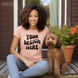 May include: A woman wearing a peach colored t-shirt with the text "YOUR DESIGN HERE" in black. She is sitting on a wooden deck with a brown dog sitting next to her.