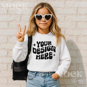 May include: A white sweatshirt with the text "YOUR DESIGN HERE" in black, worn by a person wearing heart-shaped sunglasses. The person is also wearing blue jeans and a black backpack.