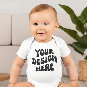 May include: A white baby onesie with the text "YOUR DESIGN HERE" in black,  with a baby wearing the onesie sitting on the floor.