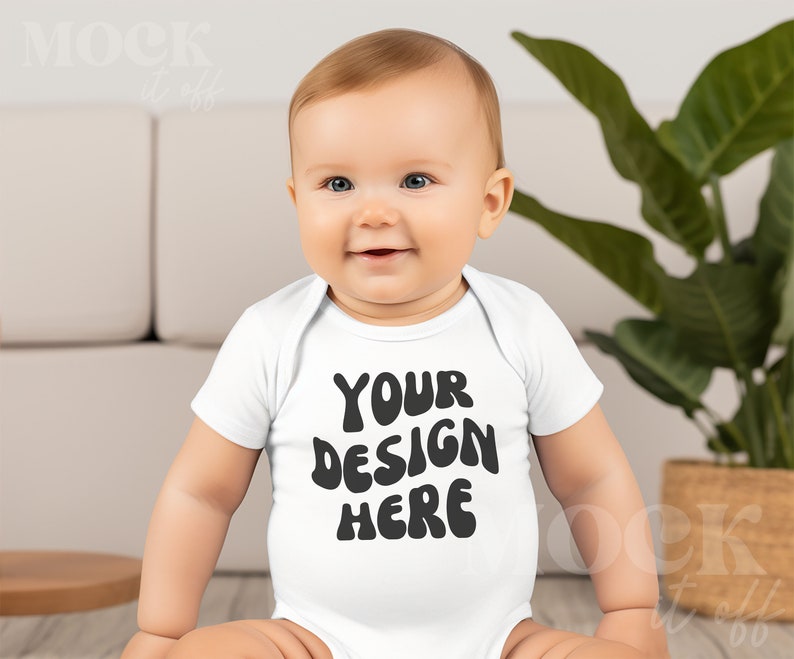 May include: A white baby onesie with the text "YOUR DESIGN HERE" in black,  with a baby wearing the onesie sitting on the floor.