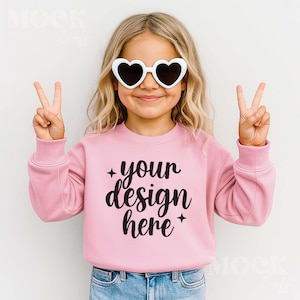 May include: A young person wearing heart-shaped sunglasses and a pink sweatshirt. The sweatshirt has the text "your design here" in black script. The person is holding up two fingers on each hand in a peace sign.