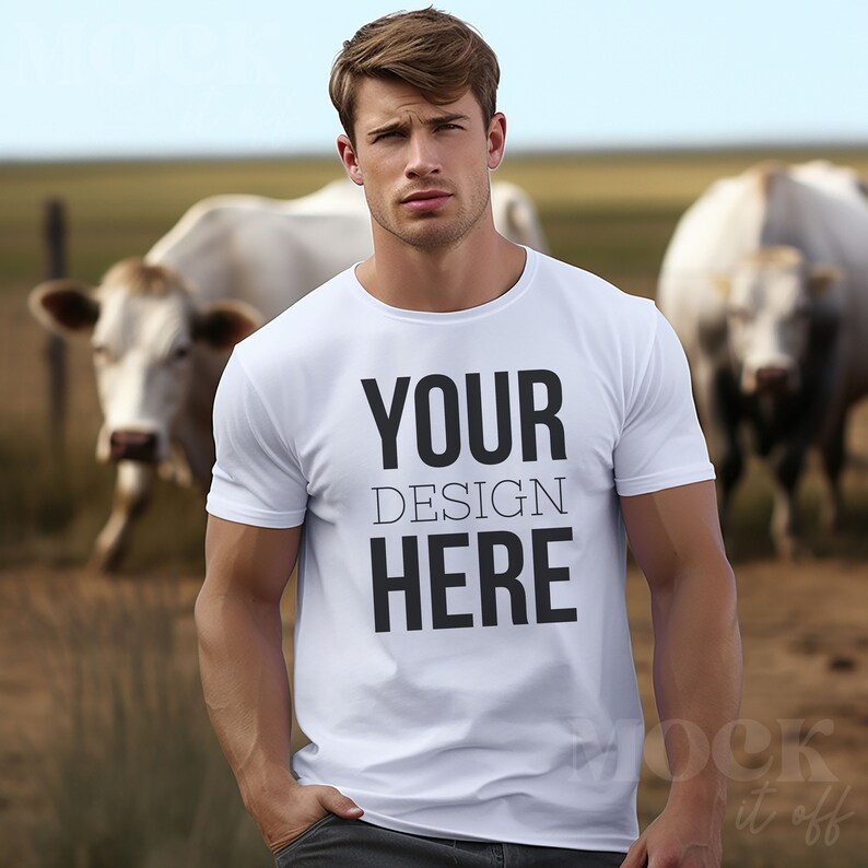 May include: White t-shirt with the text "YOUR DESIGN HERE" printed on the front. The shirt is being worn by a person standing in a field with cows in the background.