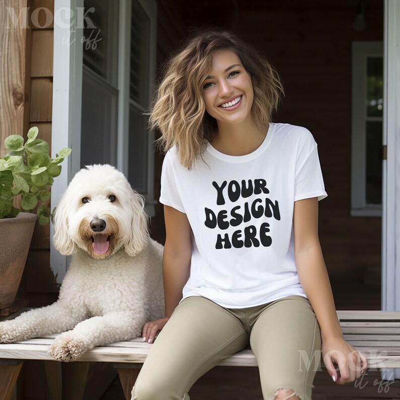 May include: A white t-shirt with the text "YOUR DESIGN HERE" in black, worn by a person sitting on a wooden bench with a white dog.