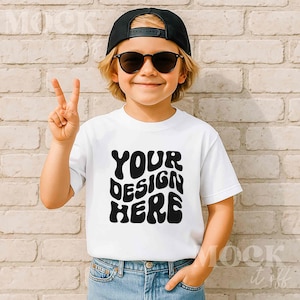 May include: A white t-shirt with the text "YOUR DESIGN HERE" in a black, retro font. The shirt is worn by a person wearing a black baseball cap and sunglasses. The person is giving a peace sign.