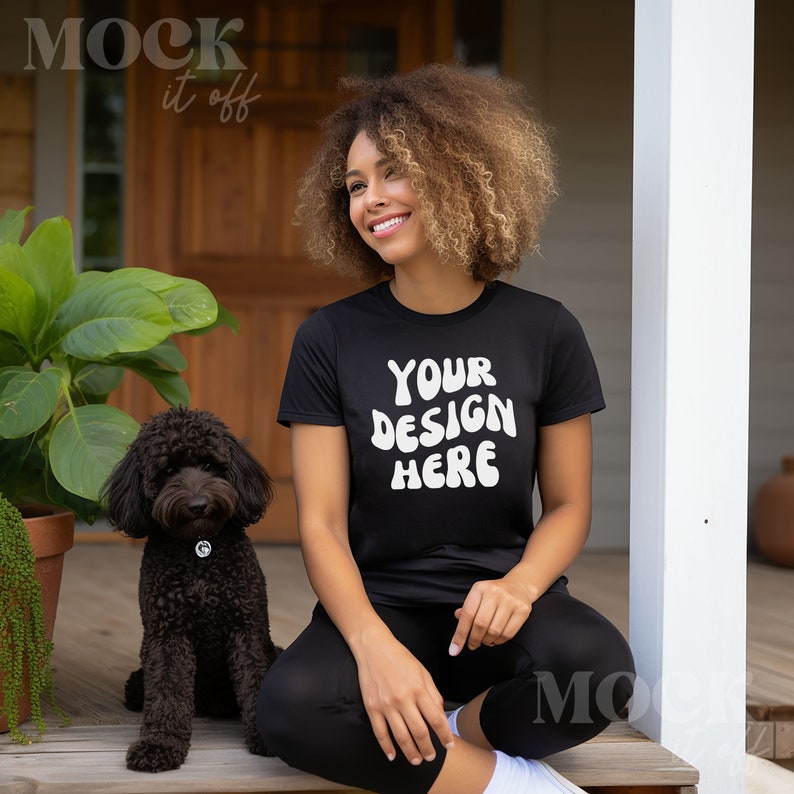 May include: A woman with curly hair is sitting on a porch with a black dog. She is wearing a black t-shirt with the text "YOUR DESIGN HERE" in white.