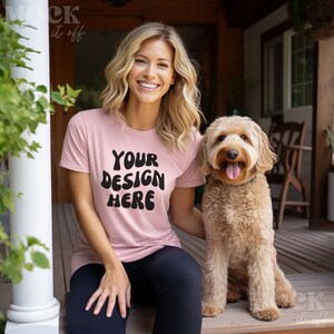 May include: A woman wearing a pink t-shirt with the text "YOUR DESIGN HERE" in black. She is sitting on a porch with a brown dog.