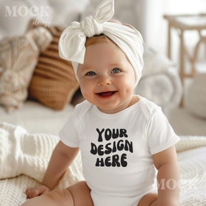 May include: A white baby onesie with short sleeves and the text "YOUR DESIGN HERE" in black. A baby is wearing the onesie and a white headband with a bow.