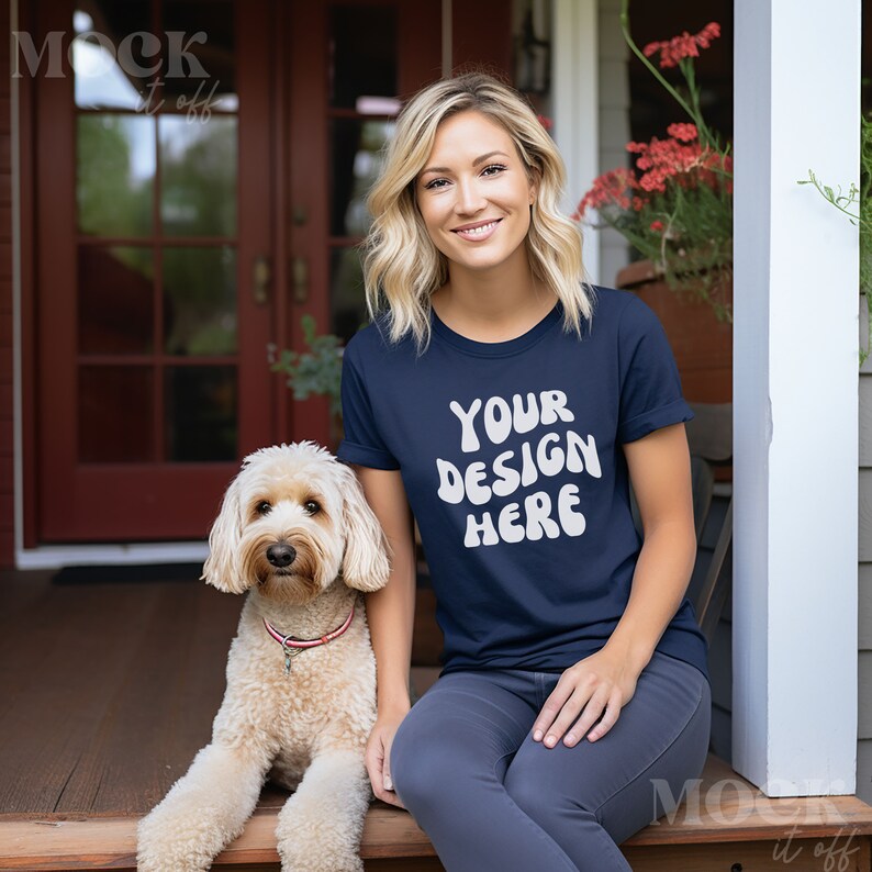 May include: A woman wearing a navy blue t-shirt with the text "YOUR DESIGN HERE" in white. She is sitting on a porch with a light brown dog.