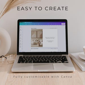 May include: A silver laptop displaying a design project presentation on its screen, with the text EASY TO CREATE above it. Beside the laptop are a white ceramic vase with dried grass, clear glasses, and a white coffee cup on a stack of books.