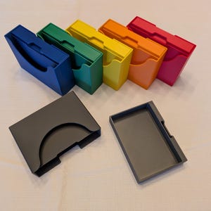 May include: Six colorful plastic storage boxes with lids, stacked in a rainbow pattern. Two additional black plastic boxes with lids are on the table.