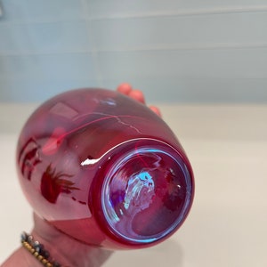 May include: A deep red glass vase with a iridescent finish. The vase is round and has a wide opening.