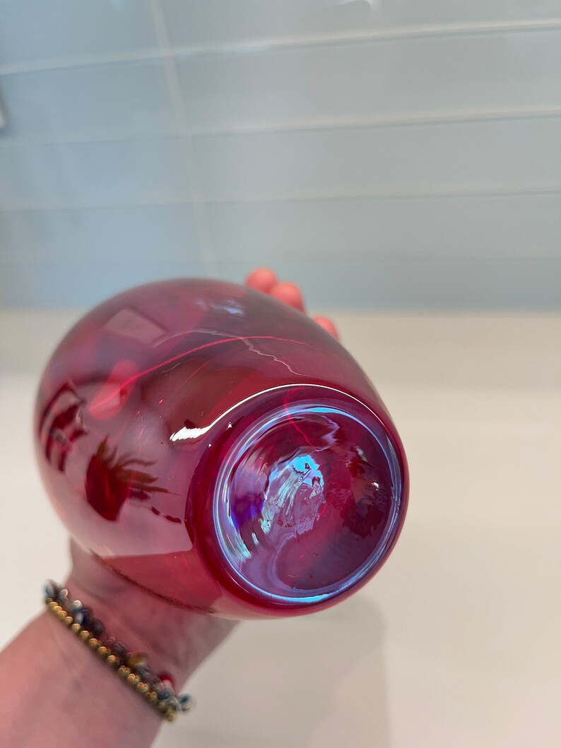 May include: A deep red glass vase with a iridescent finish. The vase is round and has a wide opening.