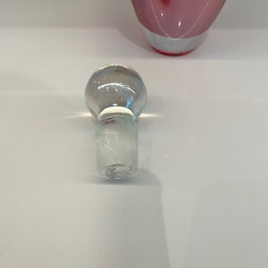 May include: A clear glass bottle stopper with a round top and a textured base. The stopper is designed to fit a bottle with a standard neck size.