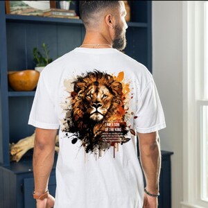 May include: White t-shirt featuring a detailed lion's head design with brown, orange, and black accents. The text "I AM A SON OF THE KING" is printed below the lion. The shirt is a casual wear item.