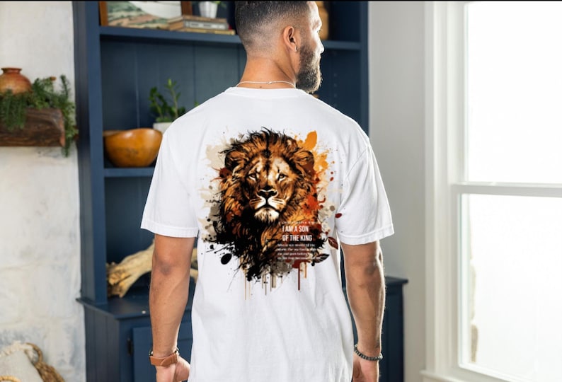 May include: White t-shirt featuring a detailed lion's head design with brown, orange, and black accents. The text "I AM A SON OF THE KING" is printed below the lion. The shirt is a casual wear item.