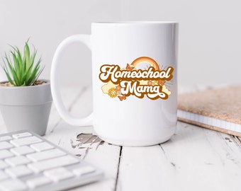 Puede incluir: Taza de cerámica blanca con un gráfico marrón y naranja que dice "Homeschool Mama" con un arcoíris, mariposas y flores.