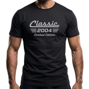May include: Black crew neck t-shirt with the text "Classic 2004 Limited Edition" in a light gray font. The text is centered on the chest. The shirt is short-sleeved.