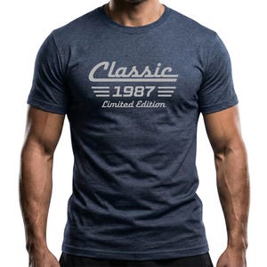 May include: Navy blue t-shirt with the text "Classic 1987 Limited Edition" in a white, stylized font. The shirt is a crew neck and has short sleeves. The overall style is casual and vintage.