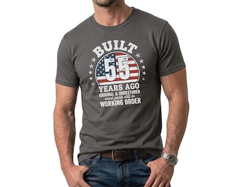 May include: Dark gray t-shirt with the text "BUILT 55 YEARS AGO ORIGINAL & UNRESTORED most parts still in WORKING ORDER" in white. The number 55 is in a red, white, and blue design, with stars around it.