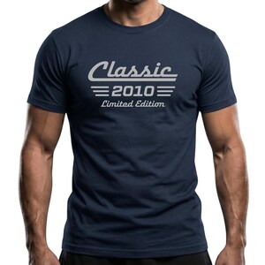 Peut inclure: T-shirt bleu marine avec l'inscription "Classic 2010 Limited Edition" en blanc, dans une police de style rétro. Le t-shirt a un col rond et des manches courtes. Le design présente le mot "Classic" au-dessus de l'année "2010".