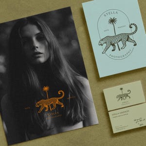 May include: A collection of stationery featuring a photography logo. The logo includes a leopard, palm tree, and the text "STELLA PHOTOGRAPHY." The stationery includes a large print, a card, and business cards, all with the same design. The color scheme is black, orange, and light blue.