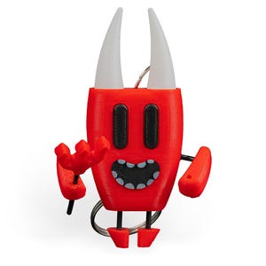 Może przedstawiać: Czerwony brelok w kształcie diabła z białymi rogami, czarnymi oczami i uśmiechniętymi ustami. Brelok ma mały, czerwony trójząb i ramiona. Nogi są również czerwone. Brelok jest przymocowany do srebrnego kółka na klucze.