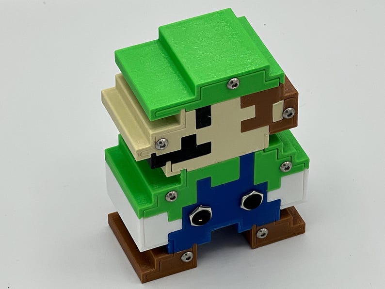 Puede incluir: Una figura pixelada y cuadrada de un personaje con gorra verde, camisa verde, peto azul y zapatos marrones. La figura est&aacute; construida con piezas de pl&aacute;stico superpuestas de varios colores, unidas por tornillos met&aacute;licos plateados visibles.