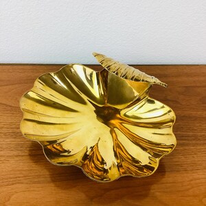 May include: A gold-colored metal dish shaped like a seashell with a leaf-shaped handle.
