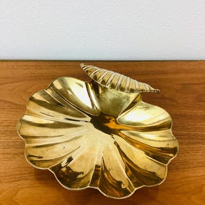 May include: A gold-colored brass dish shaped like a seashell with a decorative handle.
