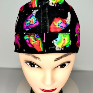 Könnte beinhalten: Eine schwarze OP-Haube mit einem farbenfrohen, abstrakten Design, das medizinische Bildgebung darstellt. Das Muster enthält lebendige Farbtöne von Rot, Gelb, Grün und Lila, die einen auffälligen Kontrast zum dunklen Hintergrund bilden. Die Haube ist so konzipiert, dass sie eng am Kopf anliegt.