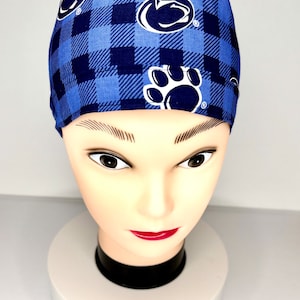 Peut inclure: Un bonnet de gommage à carreaux bleus et marine avec le logo et l'empreinte de patte des Penn State Nittany Lions. Le bonnet est présenté sur une tête de mannequin. Le bonnet est en tissu.