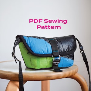 Puede incluir: Un bolso mensajero colorido con una correa y hebilla negras. El bolso presenta paneles de tela azul, verde y negra. El texto "PDF Sewing Pattern" se muestra en rosa.