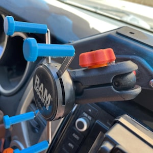 May include: A black RAM MOUNTS phone mount with a blue and silver arm and a red knob. The mount is attached to a black surface.