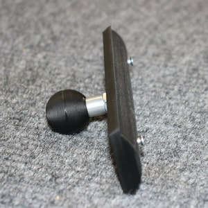 May include: A black plastic mount with a ball joint and two screws. The mount is designed to attach to a surface and hold a device.