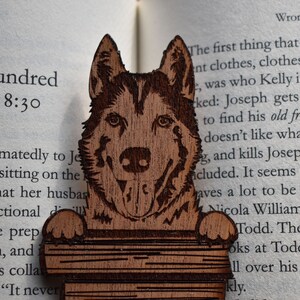 May include: Wooden bookmark featuring a detailed carving of a husky dog's head. The bookmark is holding a stack of books. The text "One Hundred -Four, 18:30" is visible in the background.