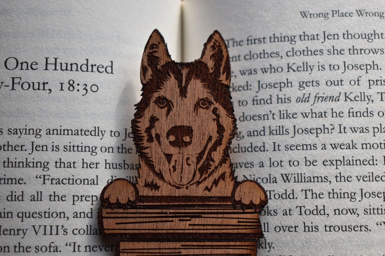 May include: Wooden bookmark featuring a detailed carving of a husky dog's head. The bookmark is holding a stack of books. The text "One Hundred -Four, 18:30" is visible in the background.