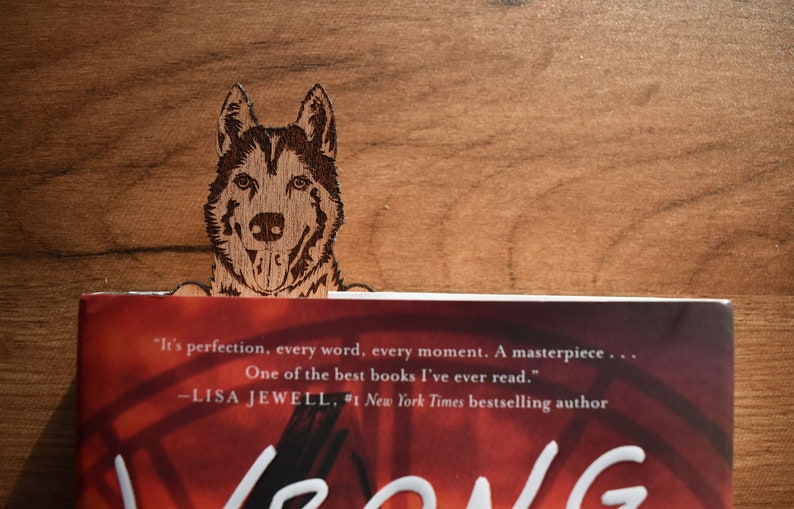 May include: A wooden bookmark featuring a laser-engraved image of a dog's head. The bookmark is placed on a book with the text "It's perfection, every word, every moment. A masterpiece... One of the best books I've ever read." -LISA JEWELL, #1 New York Times bestselling author"